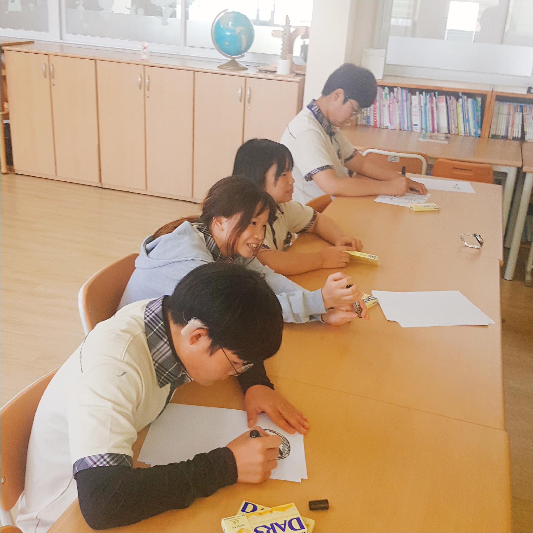 학생들이 긴 책상에 나란히 앉아 수업을 듣고 있는 사진