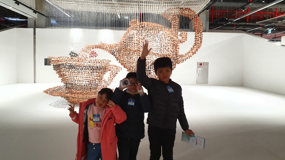 차 주전자 형상의 작품 앞에서 사진을 찍는 세 아이