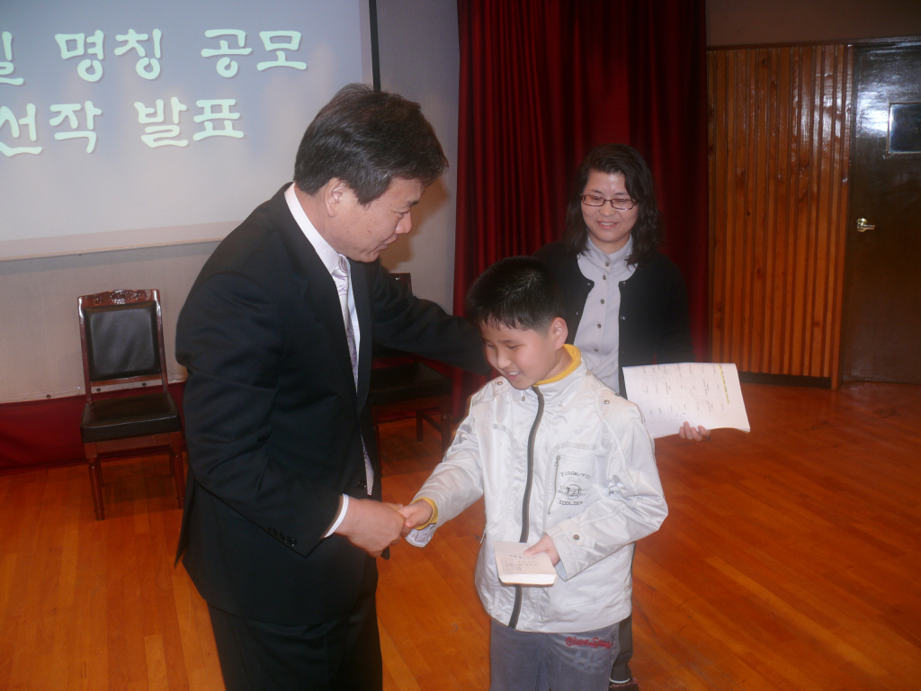 최형락 학생이 조회 중 교장선생님으로부터 당선 상금을 받고 있는 모습입니다.