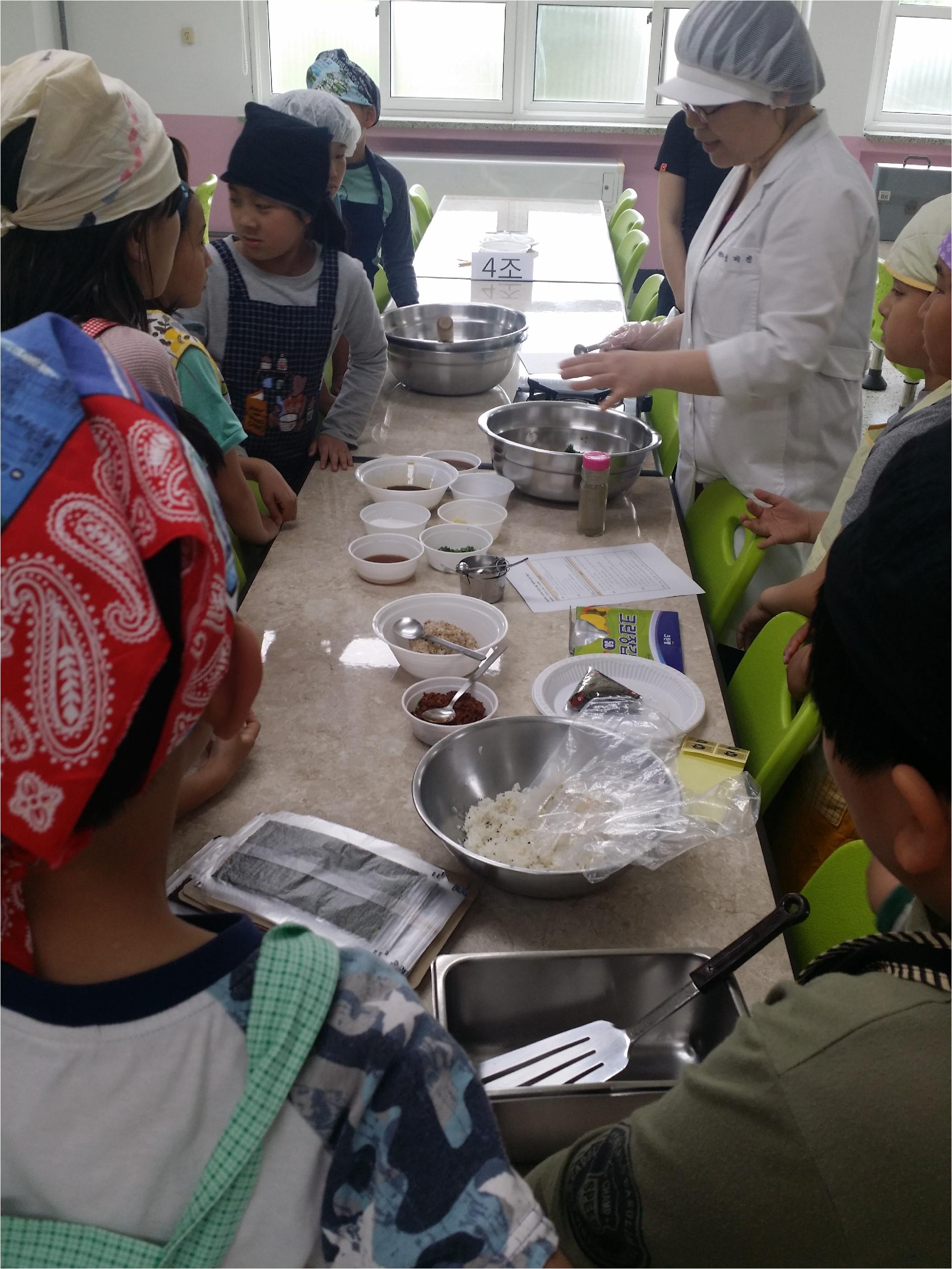 앞치마와 위생모를 착용한 4학년 아이들이 영양선생님의 말씀에 귀 기울여 듣고 있어요